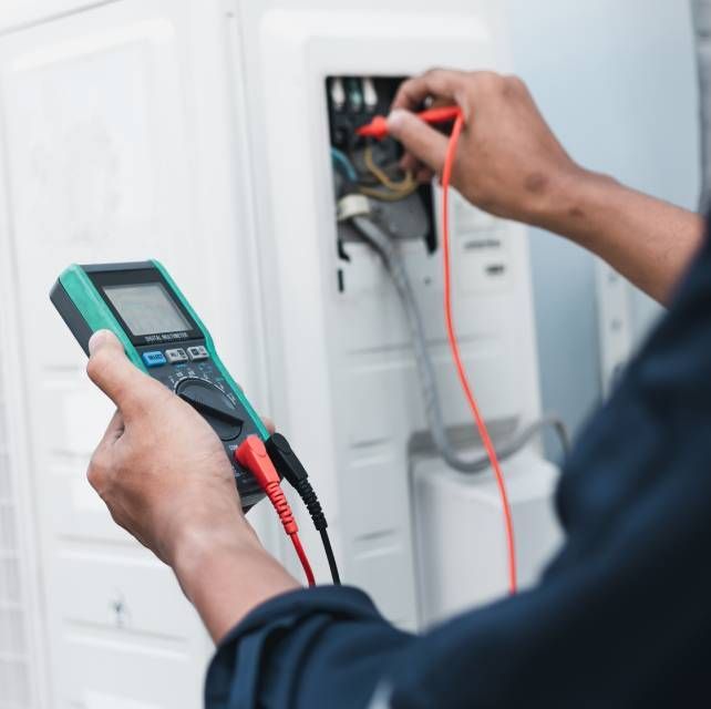 Person using a multimeter to test electrical components of an air conditioning unit.