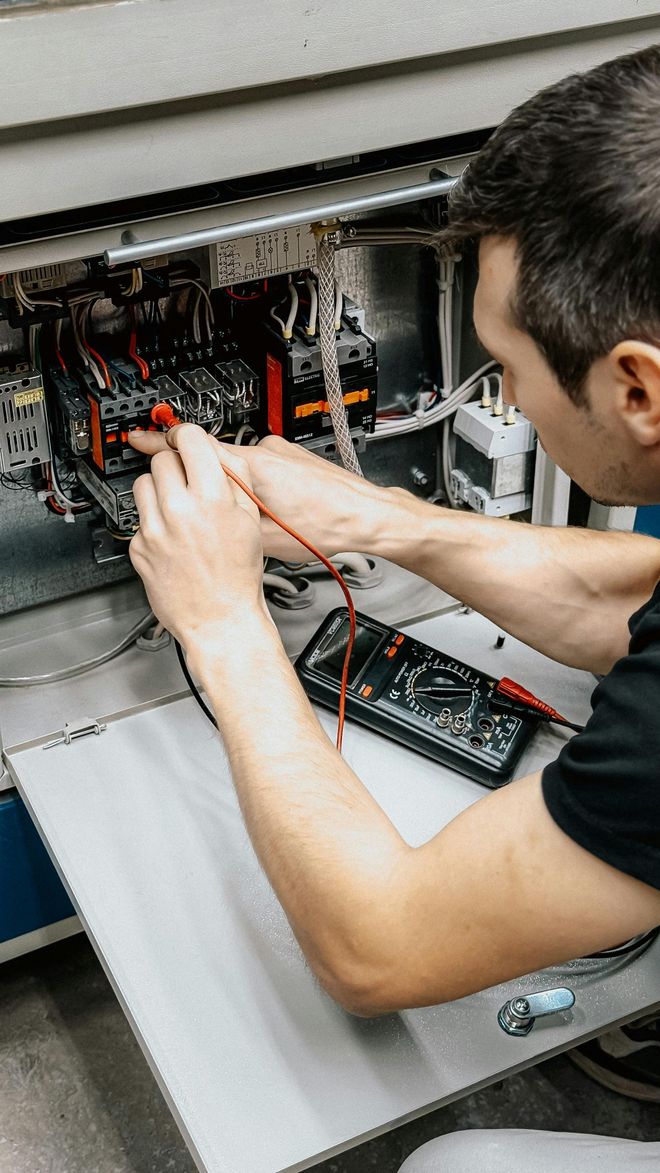 Person using a multimeter to test electrical components of an air conditioning unit.