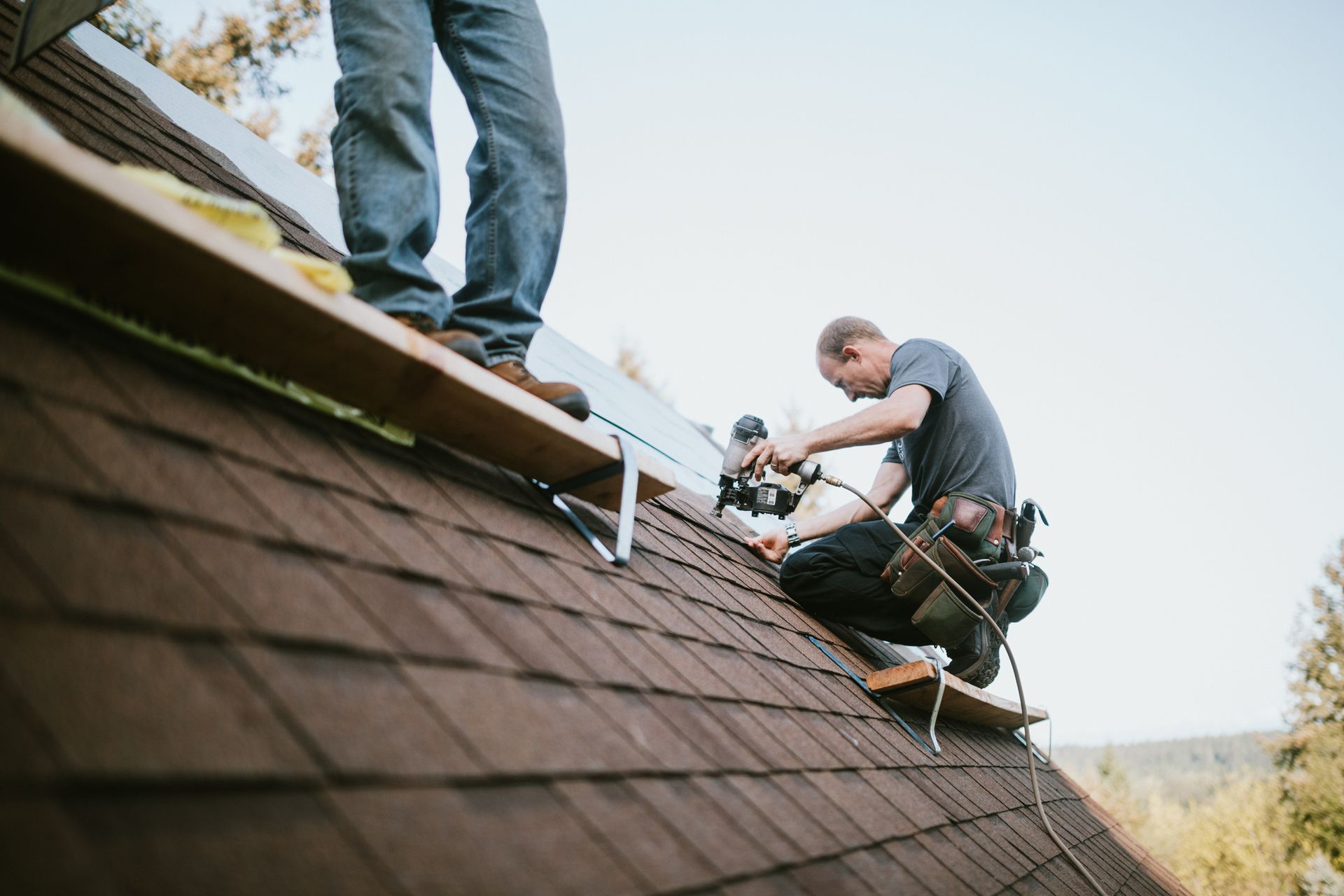 Two roofers are performing residential roof repair, putting in new roofing shingles.