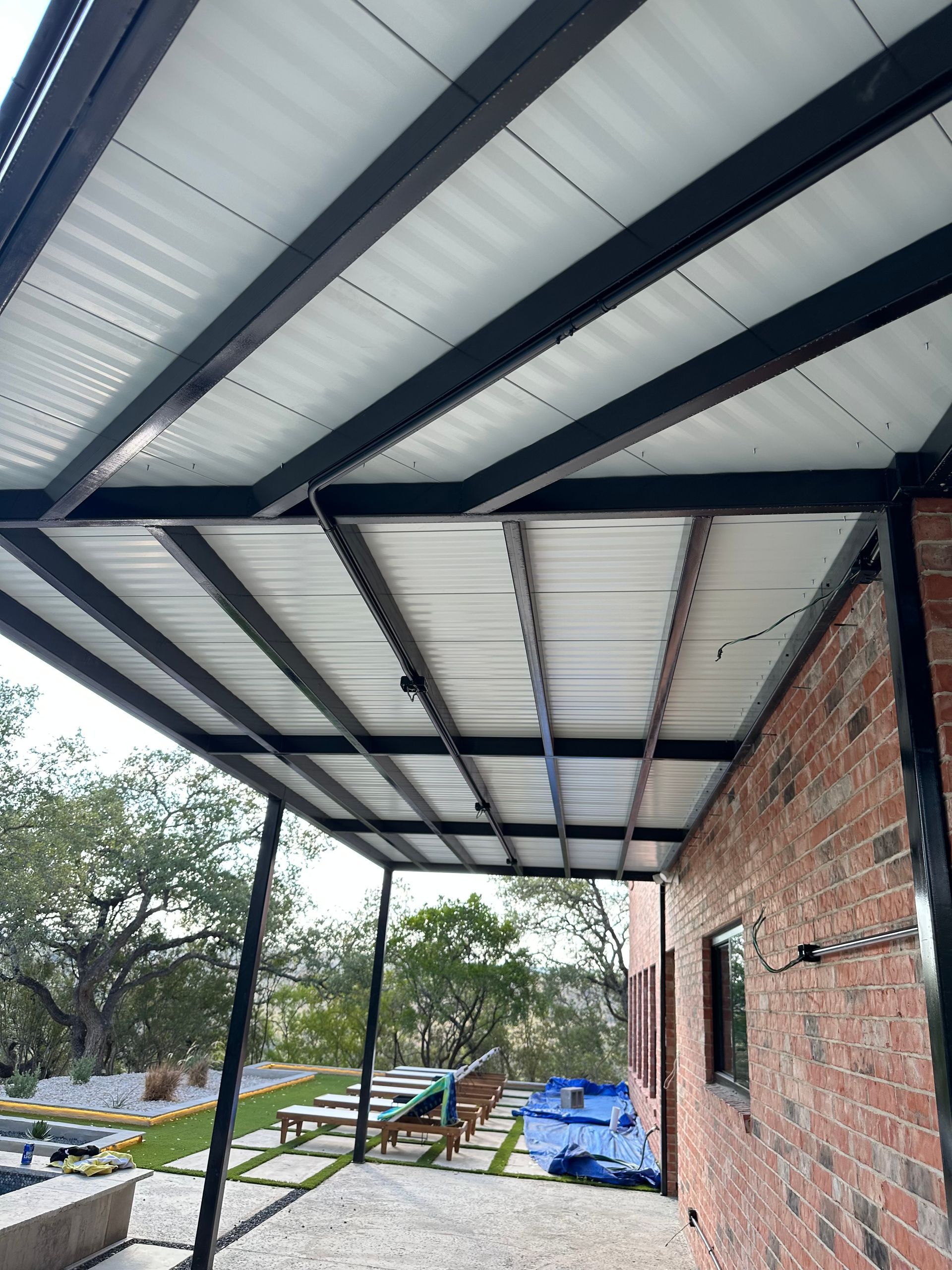 A covered patio with a white roof and a brick building in the background.