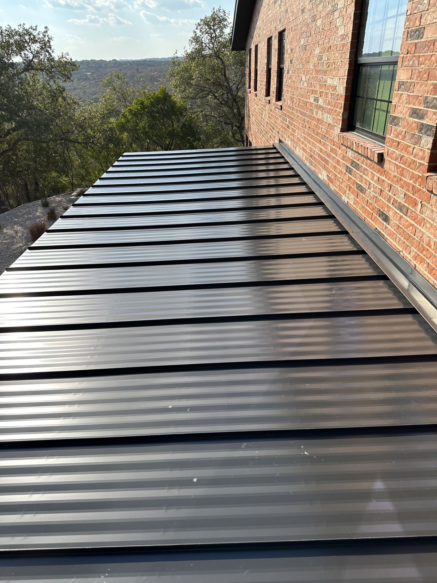 A black metal roof is on the side of a brick building.