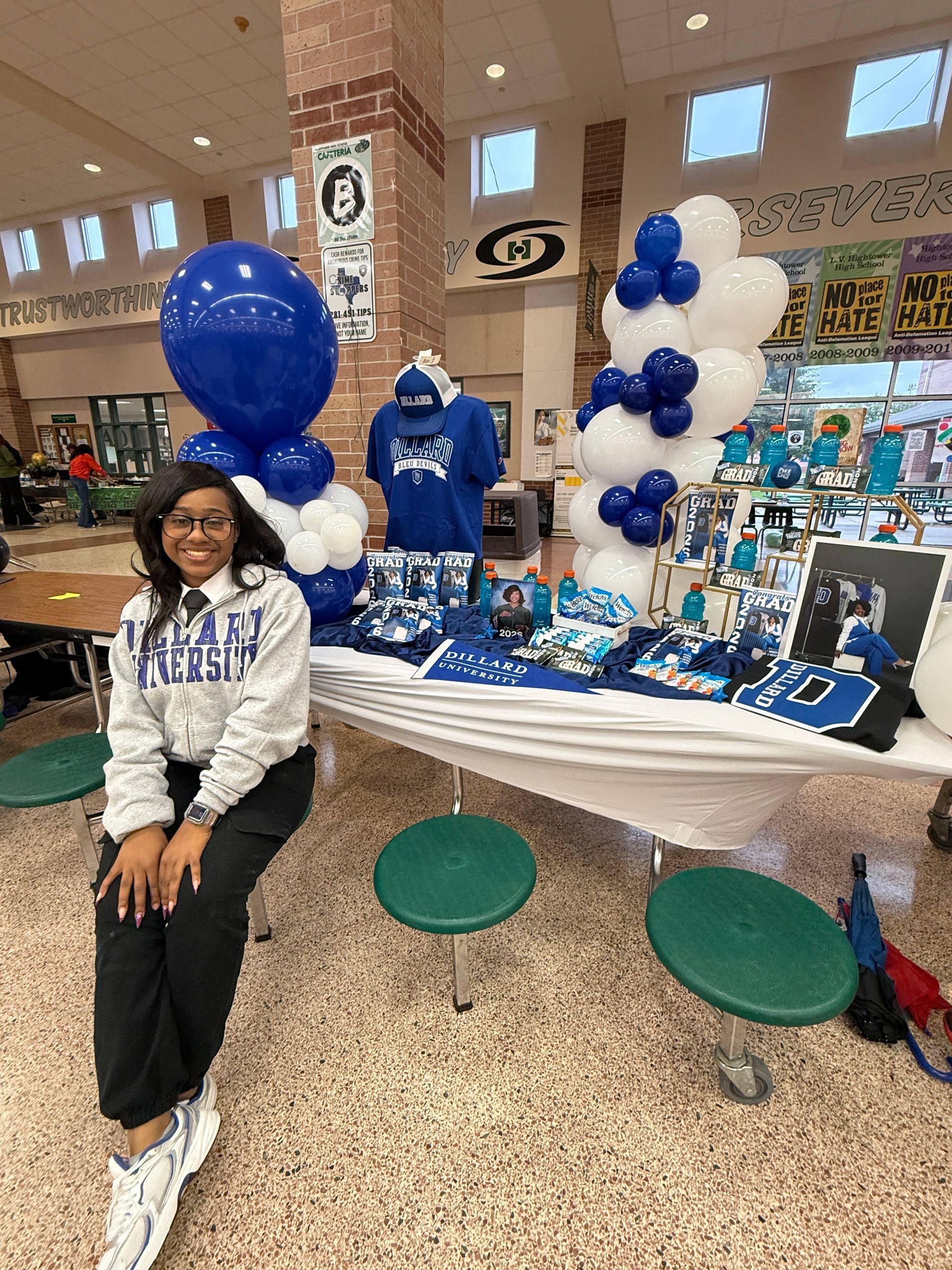 Londyn seated beside a blue-and-white balloon display at academic signing day with Dillard banners and apparel.