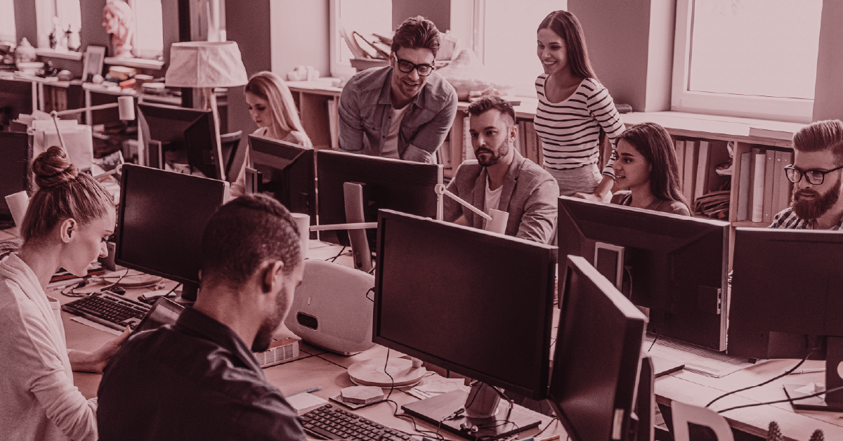Equipe de profissionais colaborando em escritório moderno com computadores, em ambiente de trabalho.