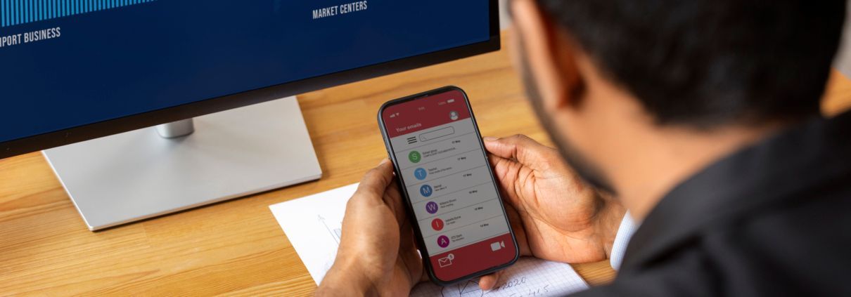 Gestão de TI em tempo real Profissional analisando e-mails no celular enquanto monitora dados em tela de computador