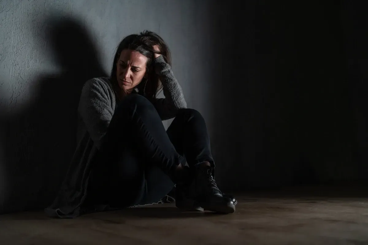 A woman is sitting on the floor in a dark room.