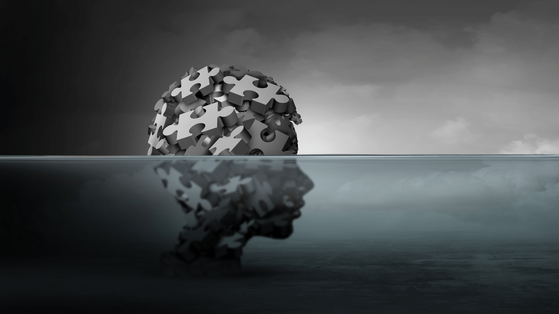 Un cervello fatto di pezzi di puzzle sopra l'acqua, riflesso come un volto umano sotto. Cielo scuro e coperto.