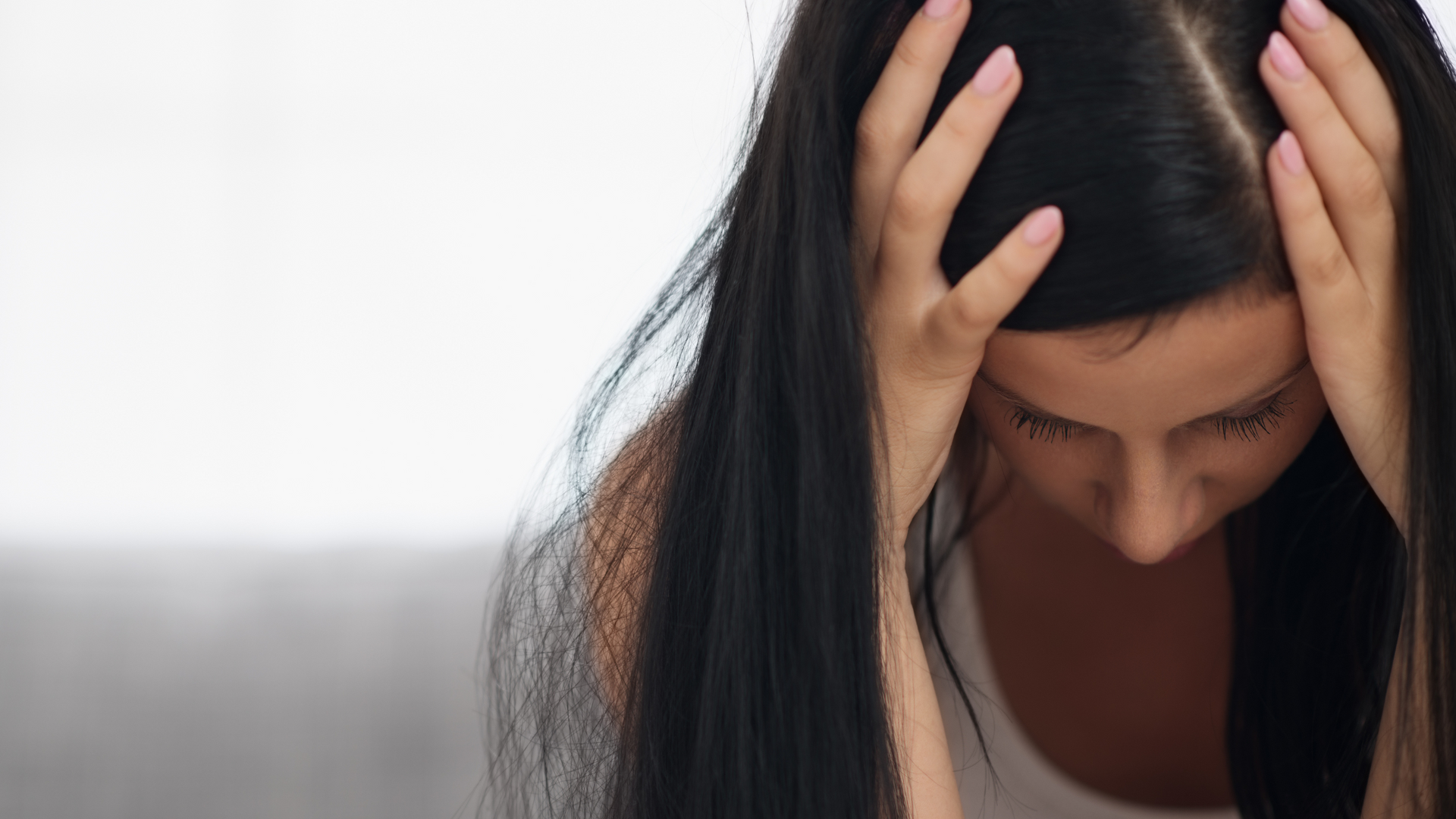 Donna con i capelli scuri, mani sulla testa, sguardo basso e espressione stressata.
