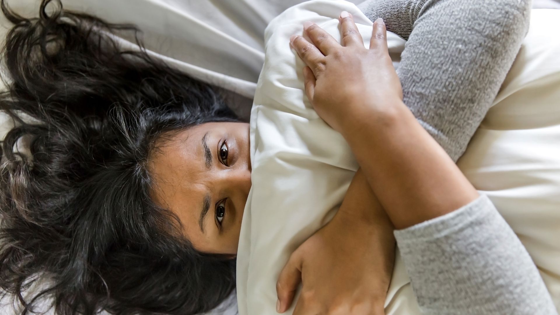 Persona che si nasconde il viso dietro un cuscino e appare ansiosa sul letto.