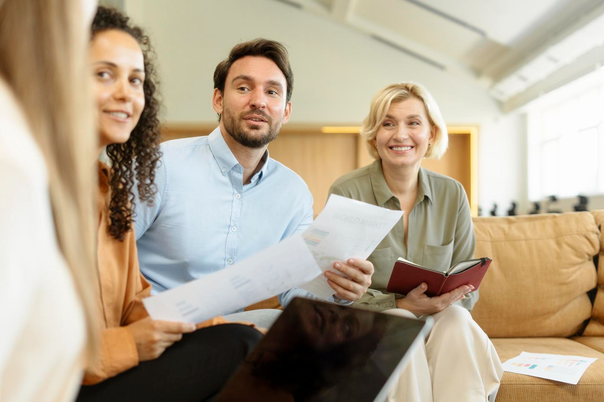 Three people reviewing papers on a couch in a bright living room