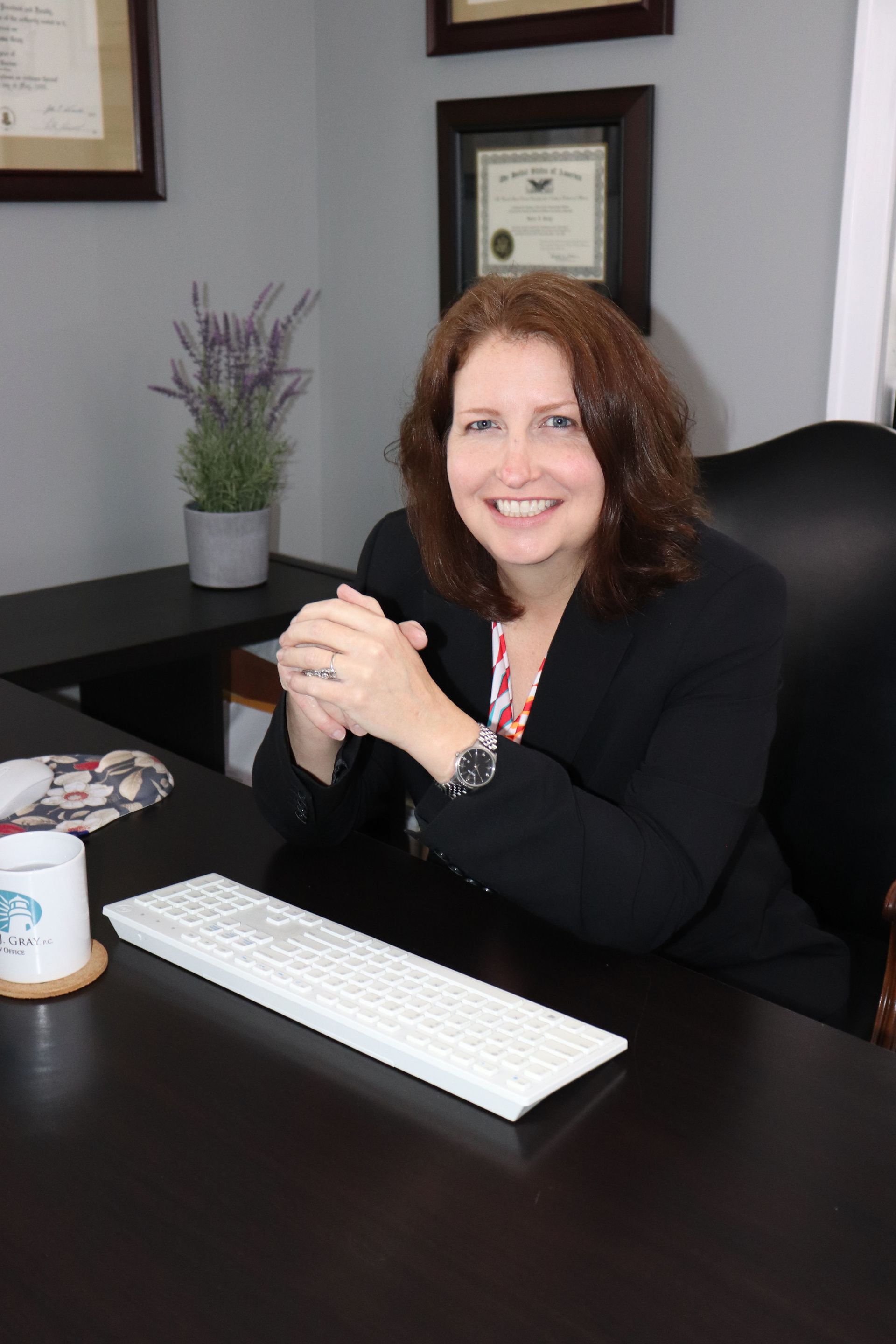 Sara J. Gray smiling at a desk in an office, with a keyboard and framed certificate behind her