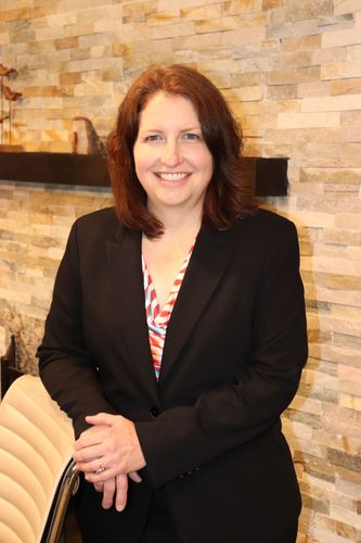 Sara J. Gray in a black blazer standing by a stone wall indoors