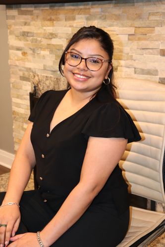 Hillary Huitron in glasses sitting on a chair against a stone wall background