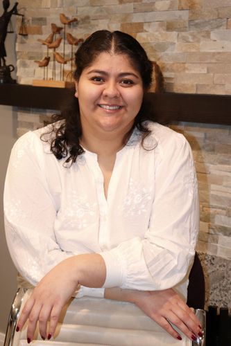 Myra Perez-Hernandez in a white blouse seated indoors against a stone wall background