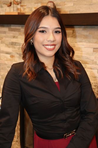 Alondra Rodriguez Angel in a black blouse and red belt smiling indoors against a stone wall.
