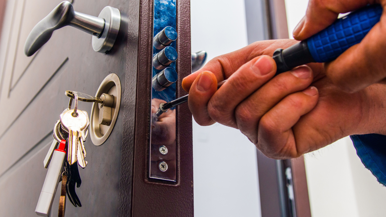 Close-up of a person using a screwdriver on a door lock. A key ring with keys hangs in the lock.