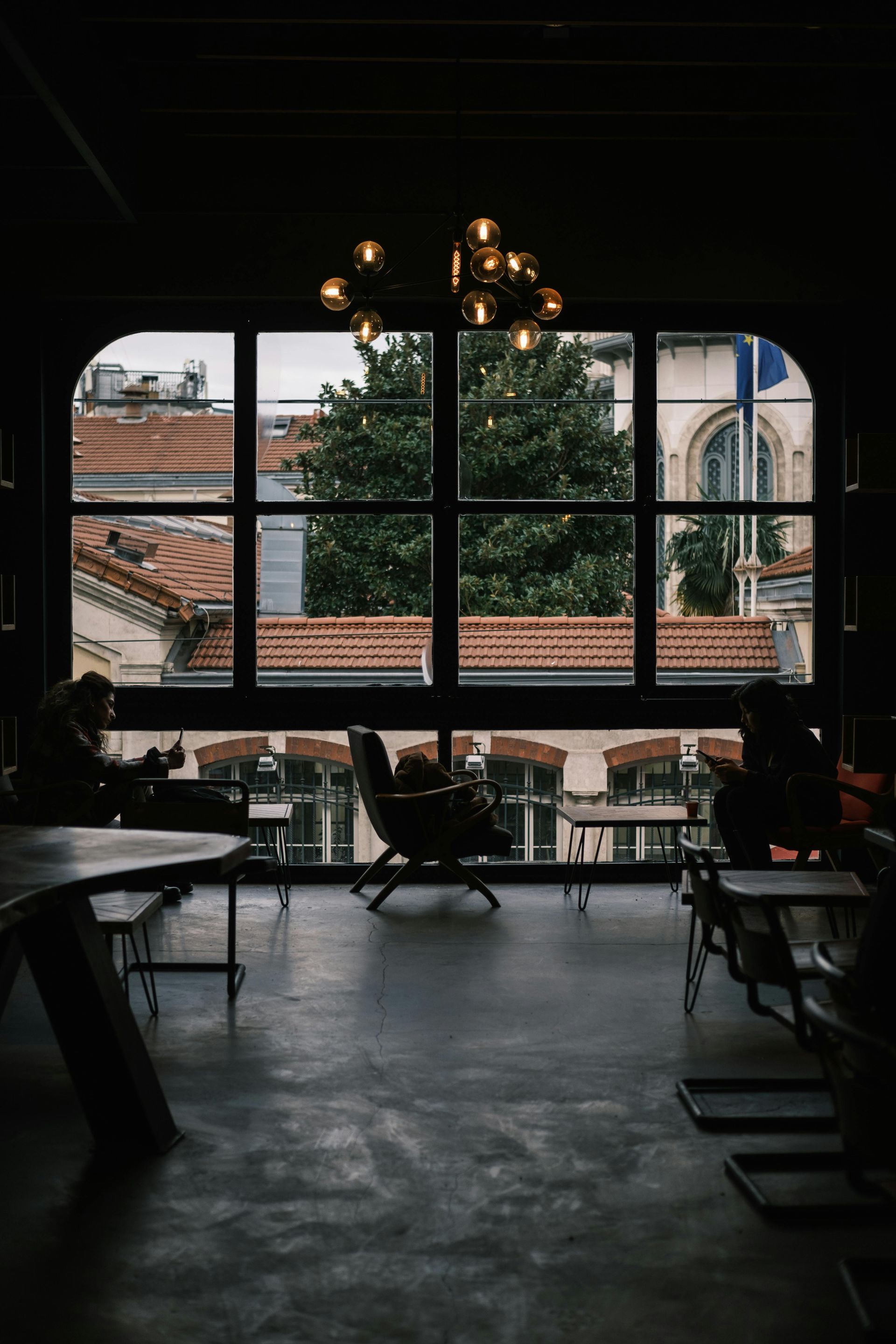 Interior with large arched window overlooking rooftops; people sit at tables.