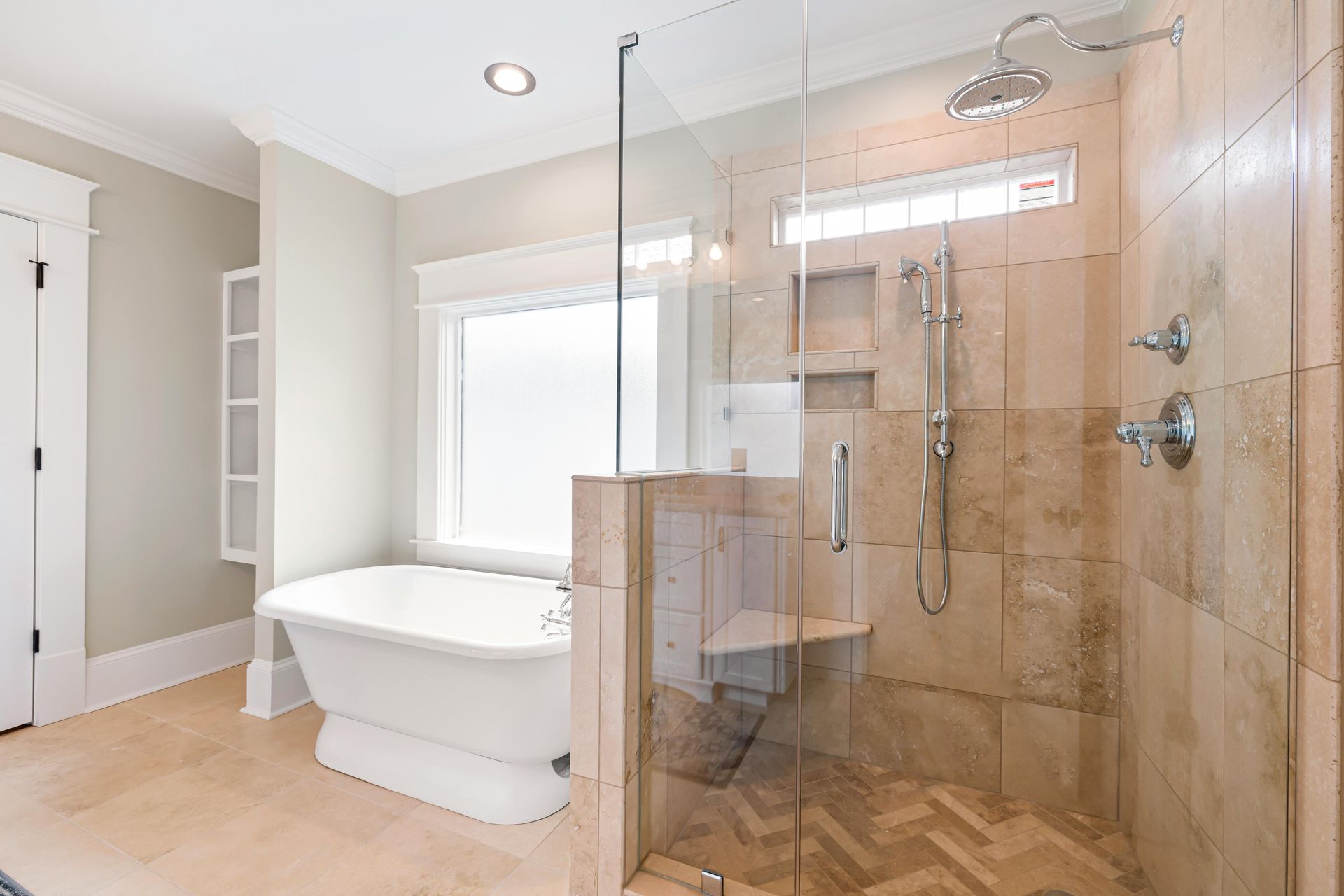 Spacious bathroom with glass-enclosed shower, freestanding tub, neutral-toned walls, and large window.
