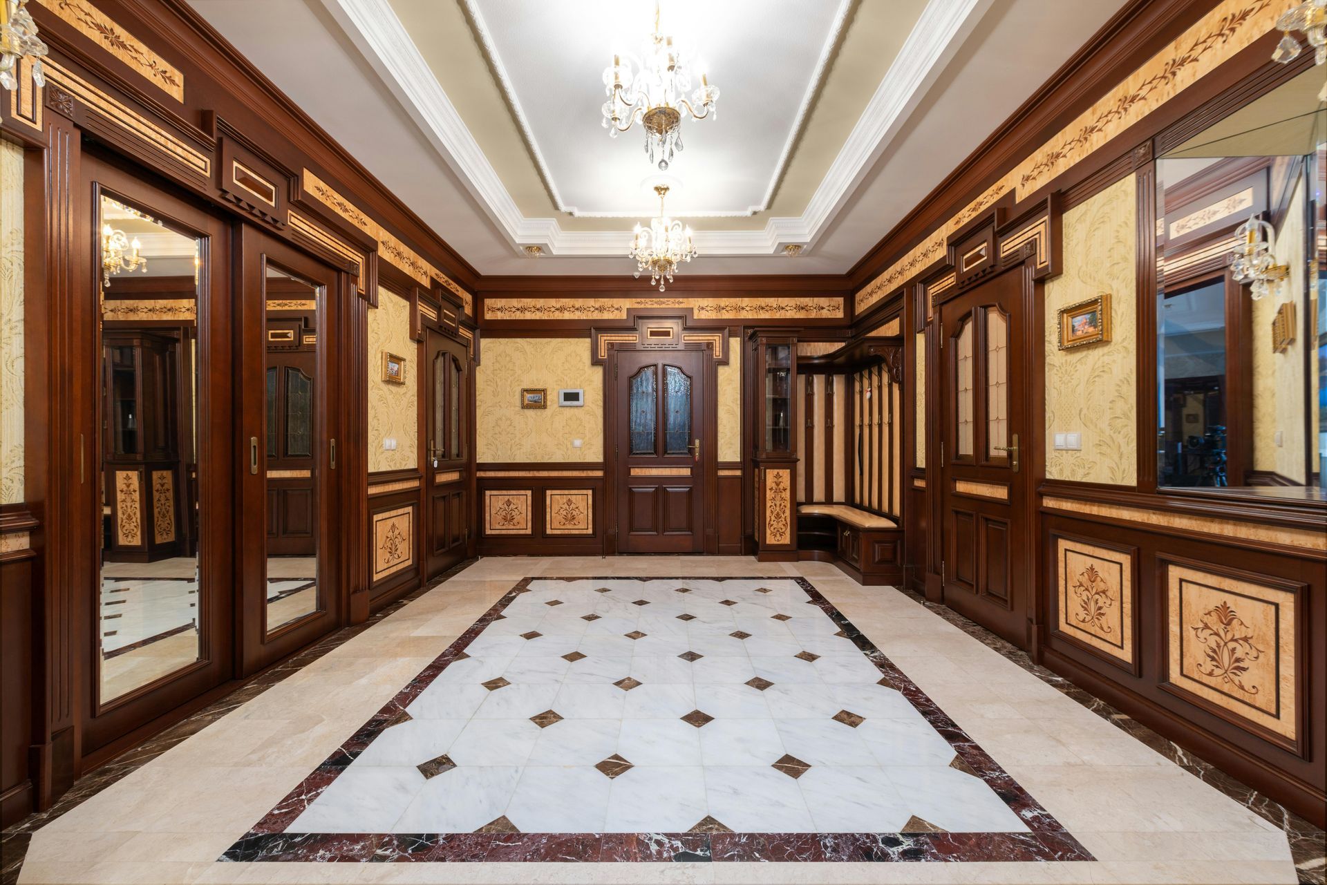Luxurious hallway with dark wood paneling, ornate tile floor, and chandeliers.