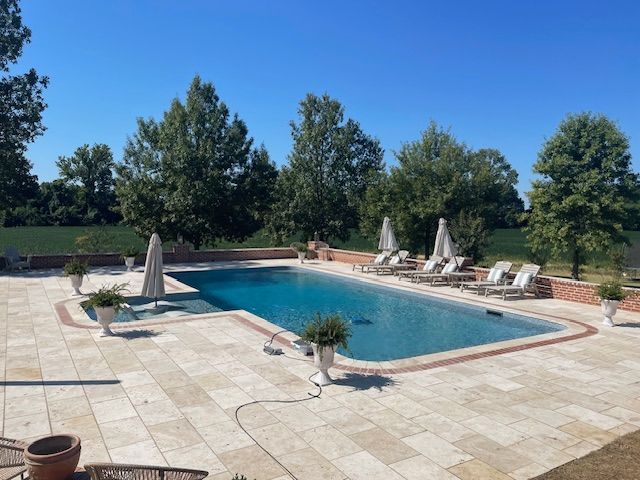 Swimming pool with lounge chairs on a paved patio on a sunny day. 
