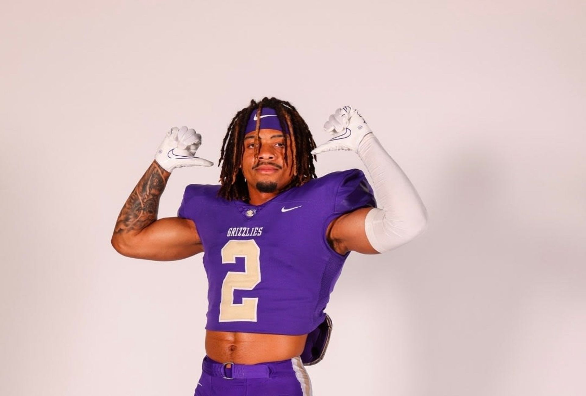 Football player in a purple jersey flexing both arms against a plain background