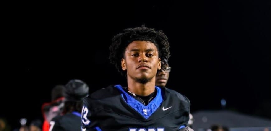 Football player in black uniform with blue accents, standing on the field at night with a focused expression