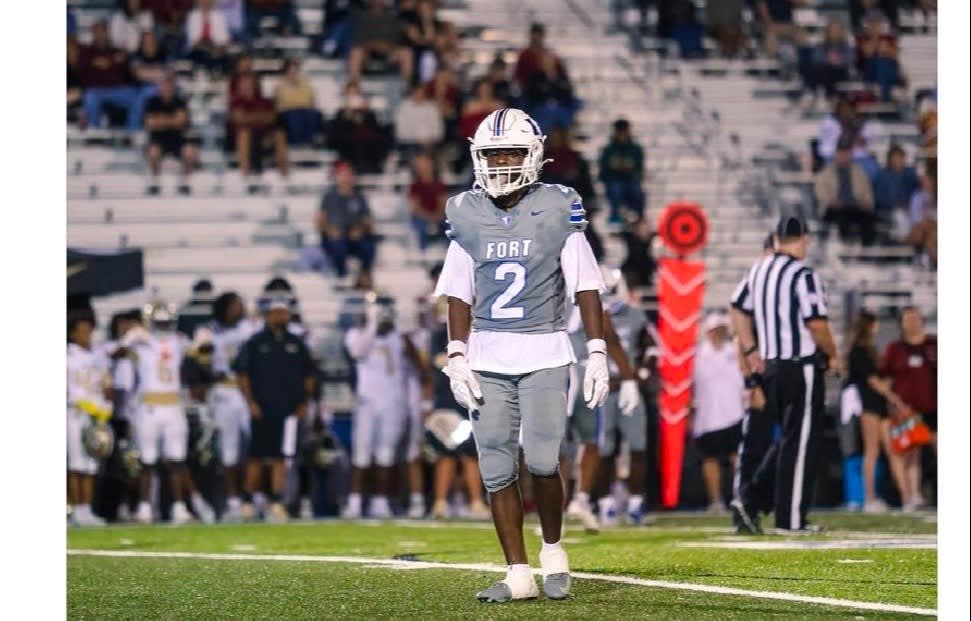 Football player in gray uniform stands on the field with sideline and crowd behind him