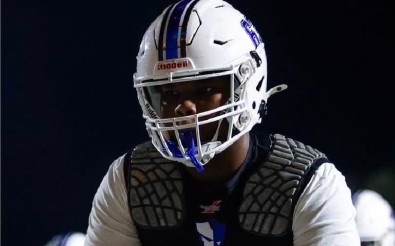Football player in white helmet and black shoulder pads against a dark background