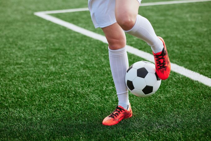 Soccer player in white socks and red cleats kicking a black-and-white ball on a green field