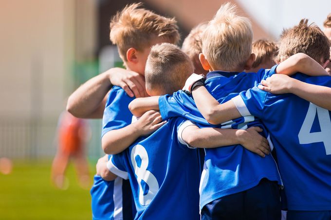 Youth soccer players in blue jerseys huddle together on a sunny field