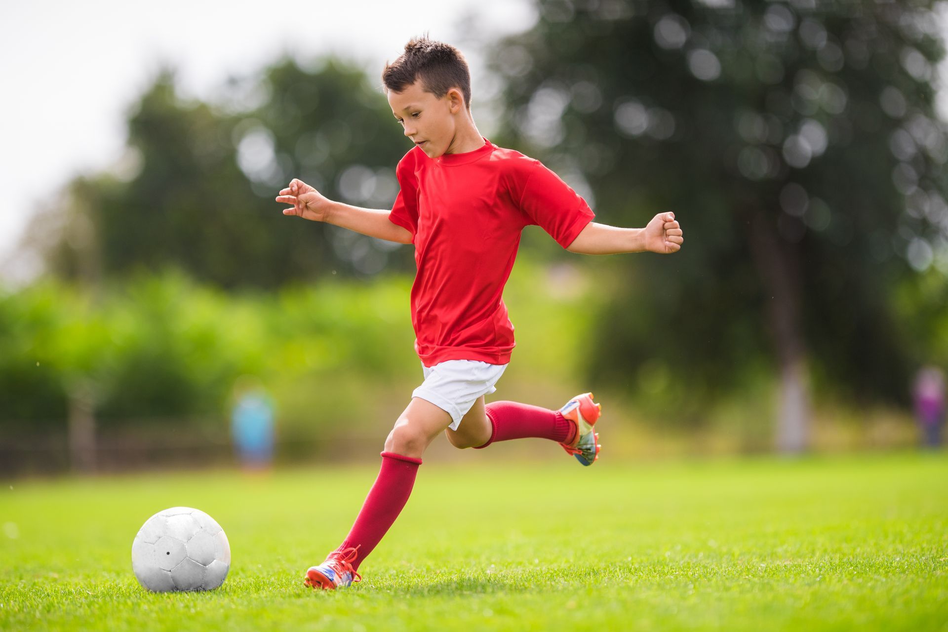 Soccer player in red kicks a ball on a grassy field