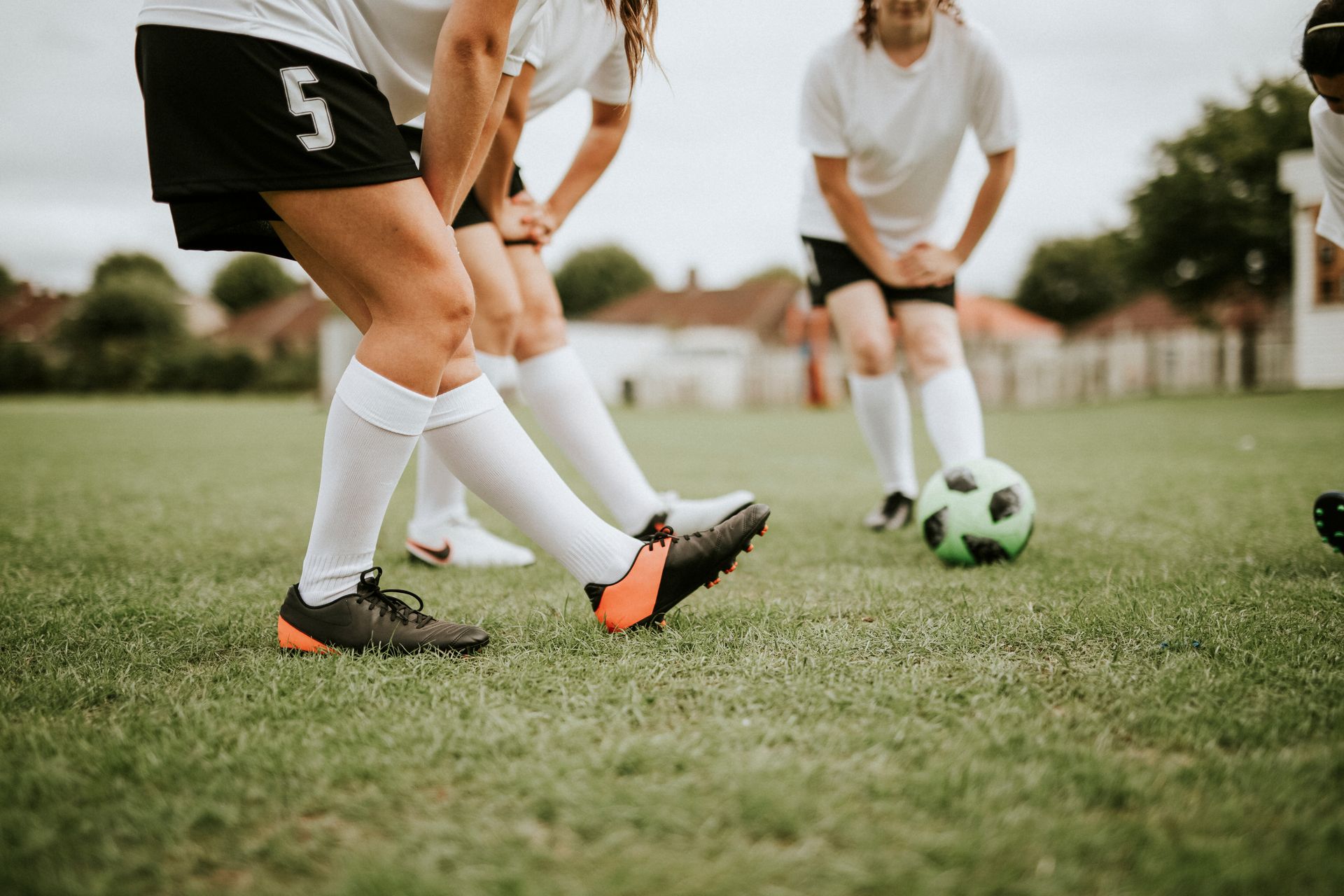Soccer players in white jerseys and black shorts on a grassy field, one kicking a green ball