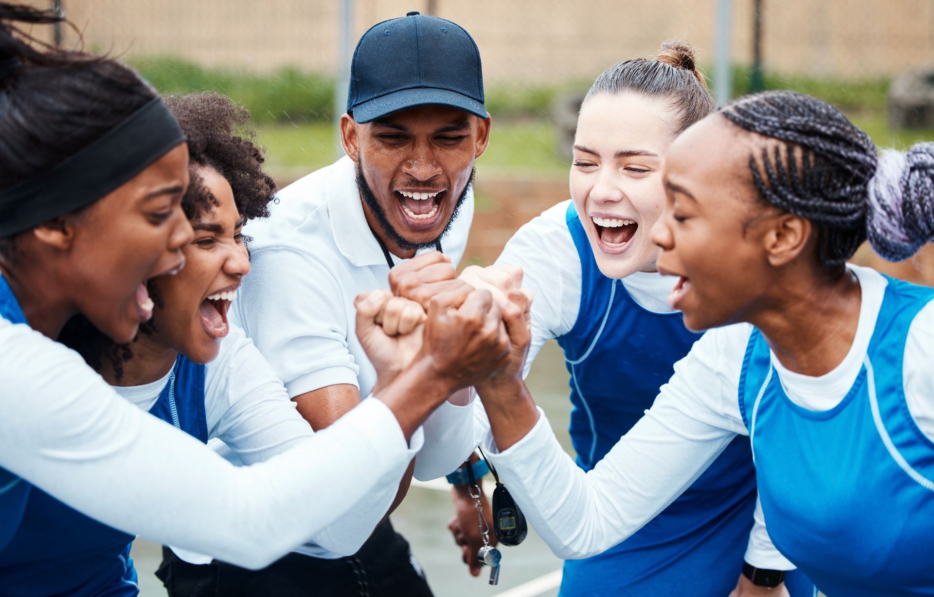 Group of athletes in blue jerseys smiling and clasping hands together outdoors