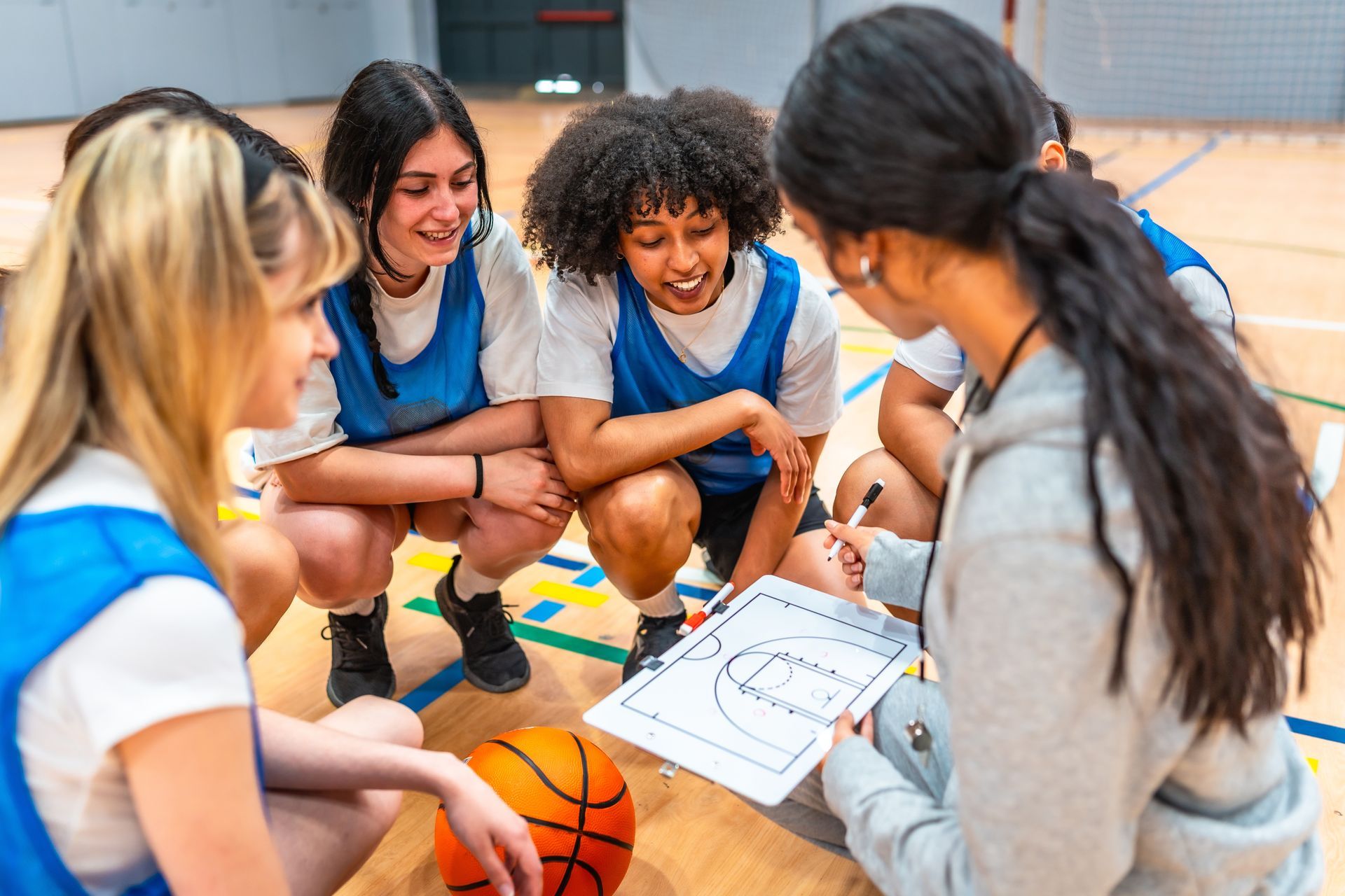Basketball team huddles around a coach with a clipboard on an indoor court