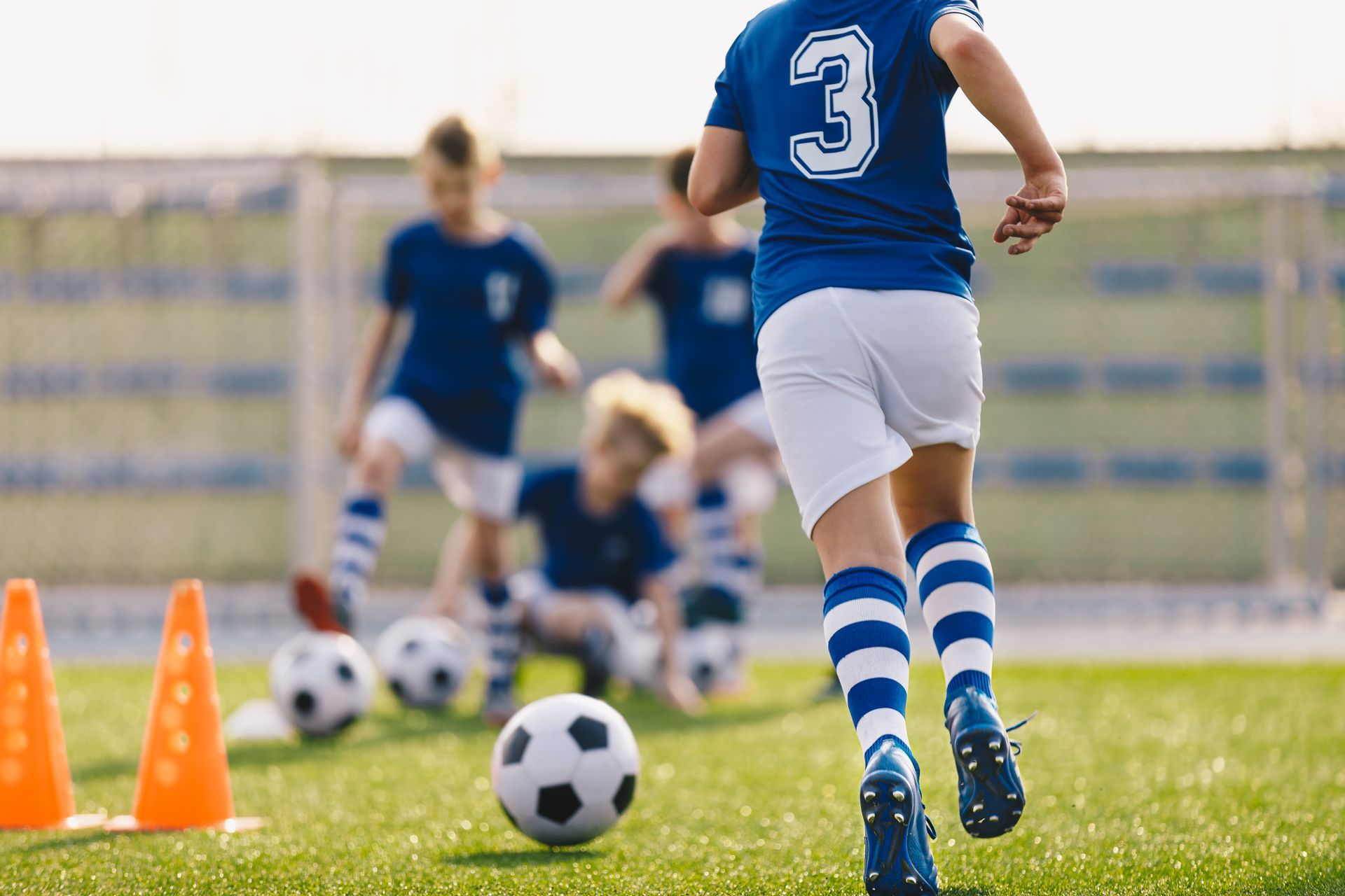 Youth soccer practice with players dribbling balls around orange cones on a grassy field