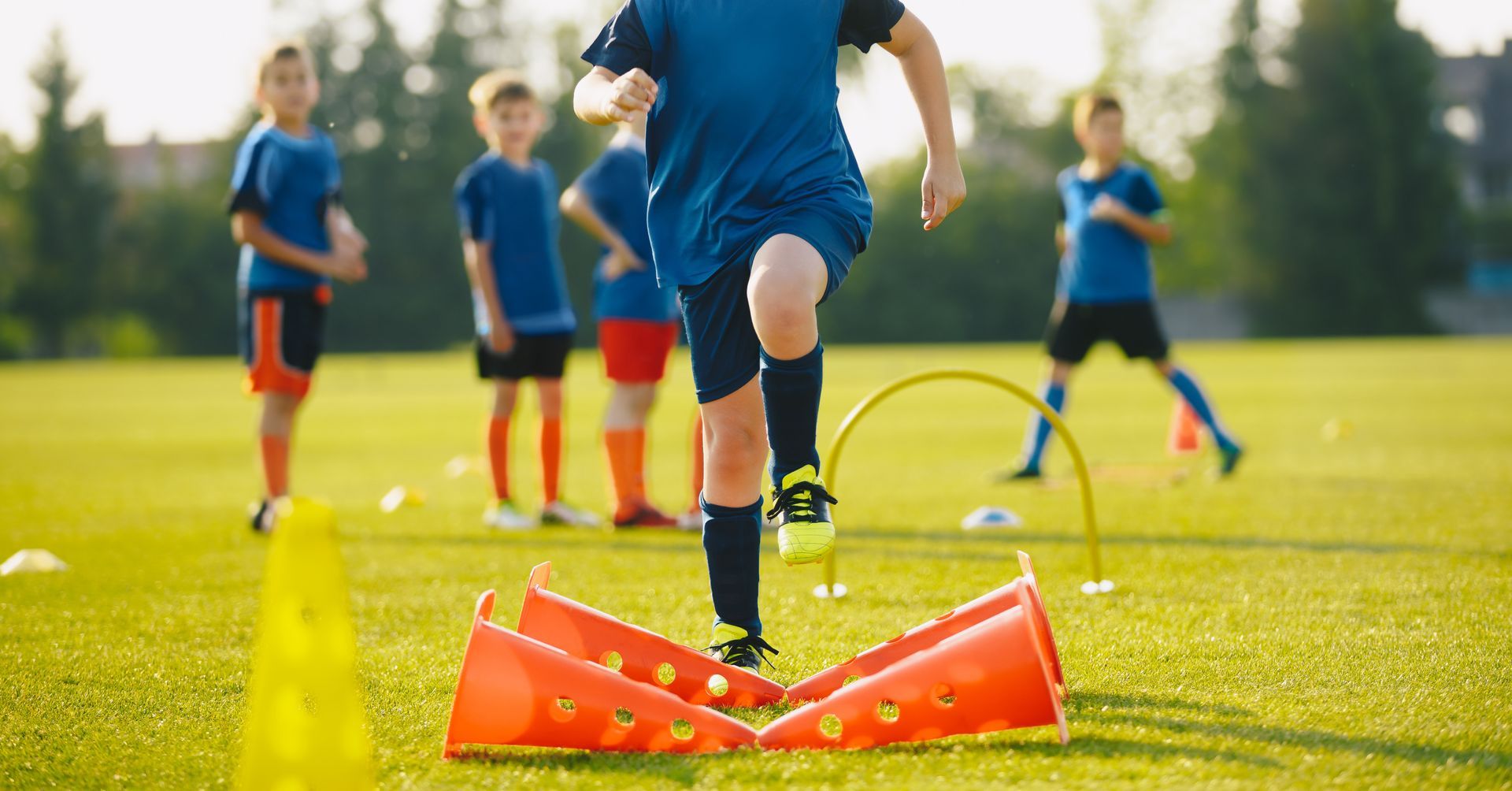 Youth soccer practice with children running agility drills around orange cones on a sunny field