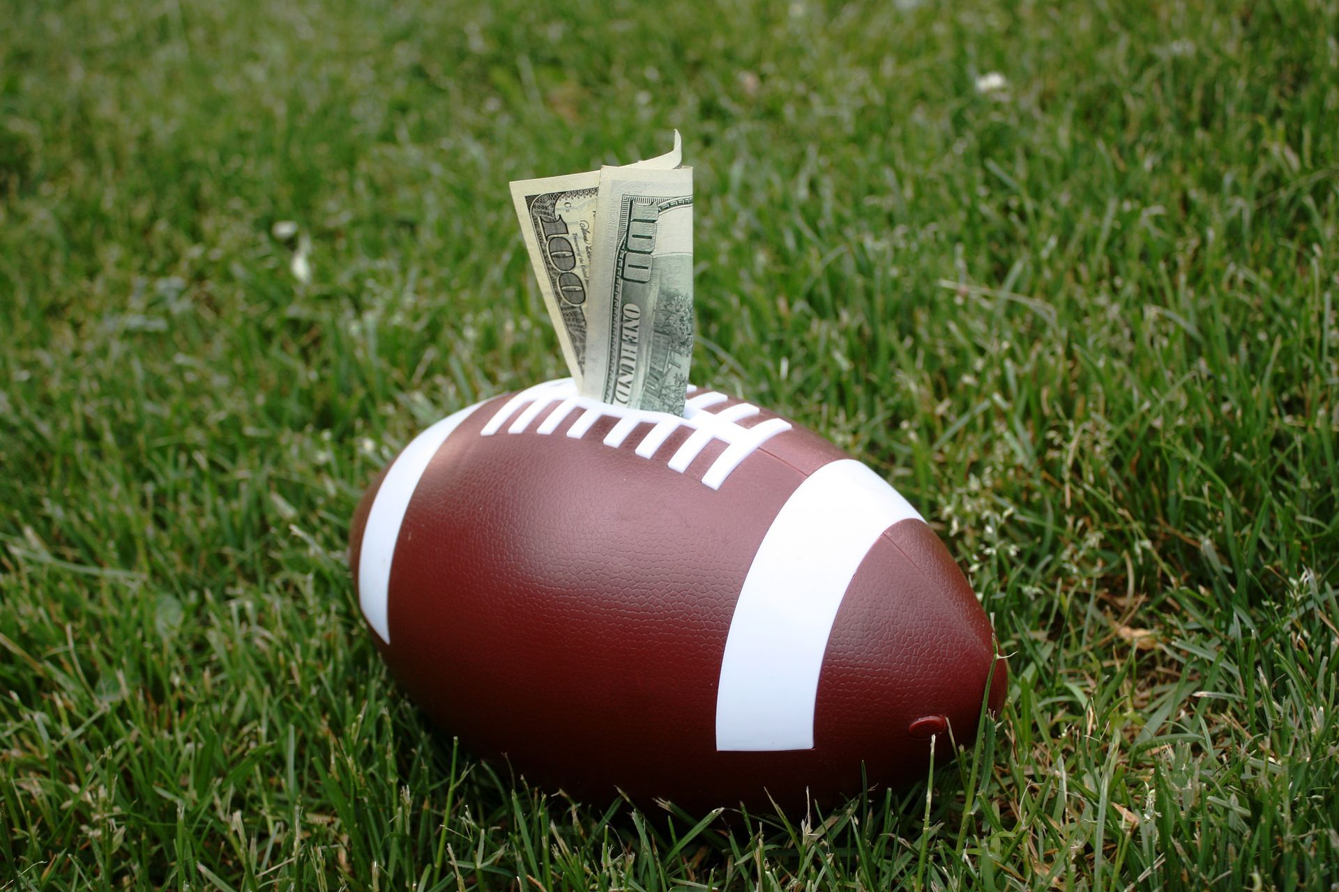 Football on grass with a dollar bill tucked into the laces
