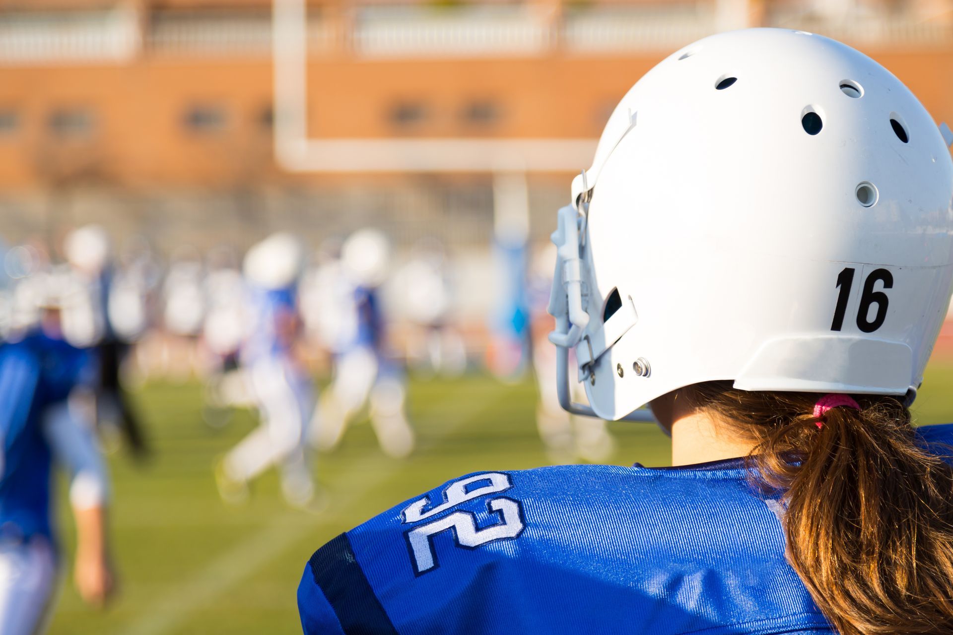 Football player in blue jersey and white helmet watching a game on the field