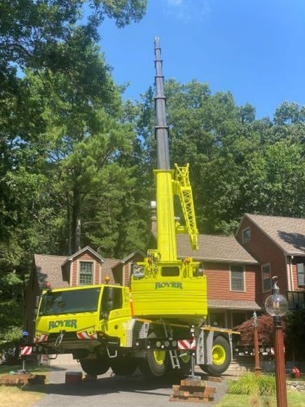 Yellow crane truck with extended boom in a residential driveway.