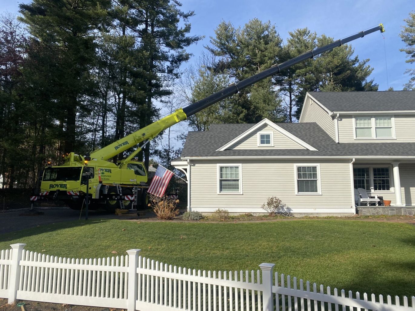 Yellow crane next to a house with a raised boom. White picket fence in front.