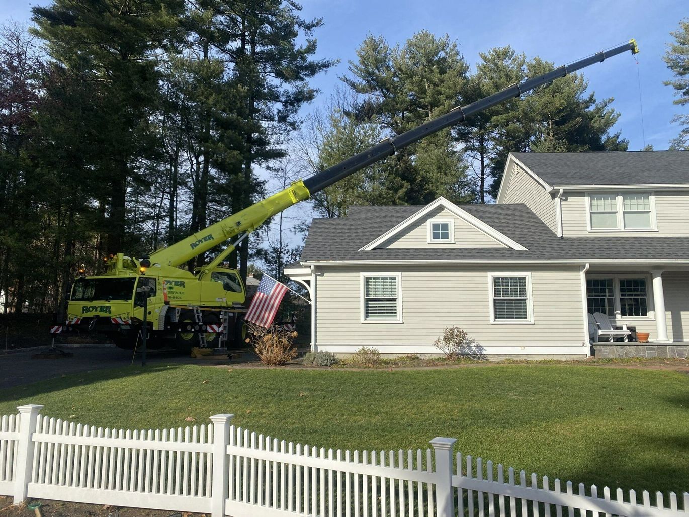 A large yellow crane positioned near a two-story house with trees in the background.