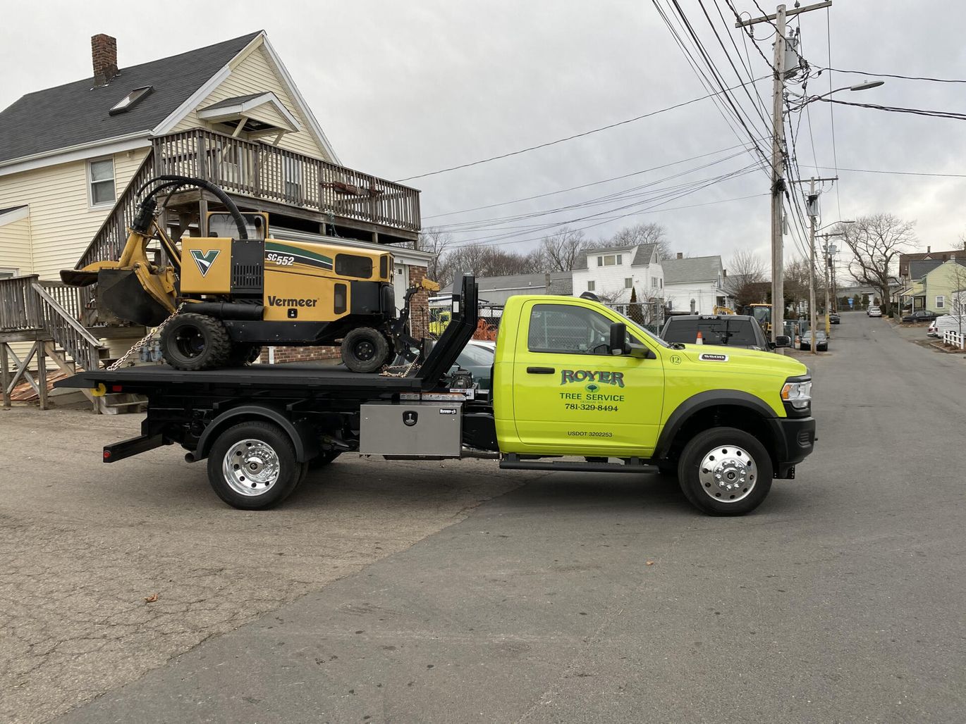 Yellow truck with a stump grinder on its flatbed parked on a street.