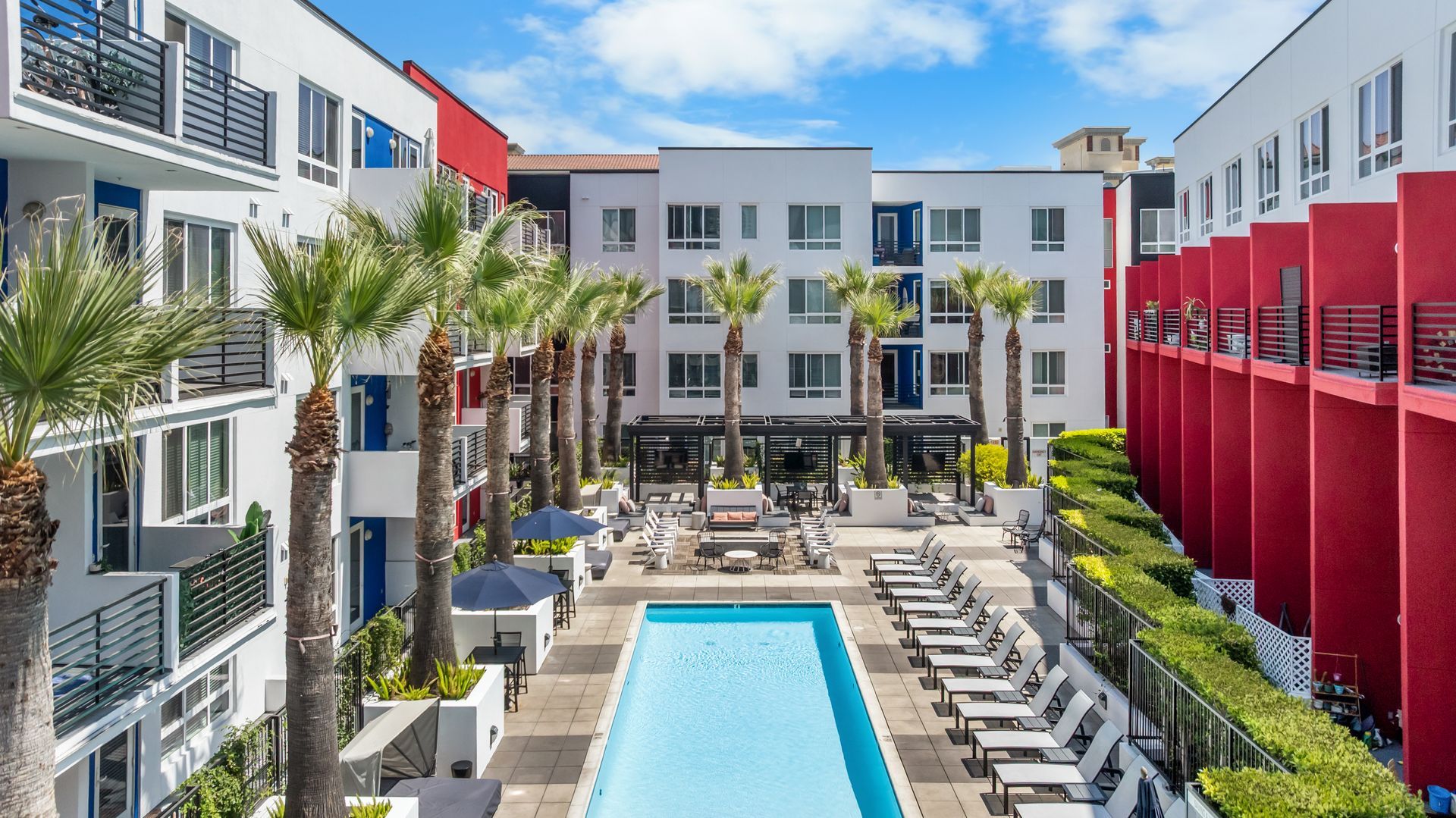 A swimming pool in a courtyard surrounded by lounge chairs and palm trees