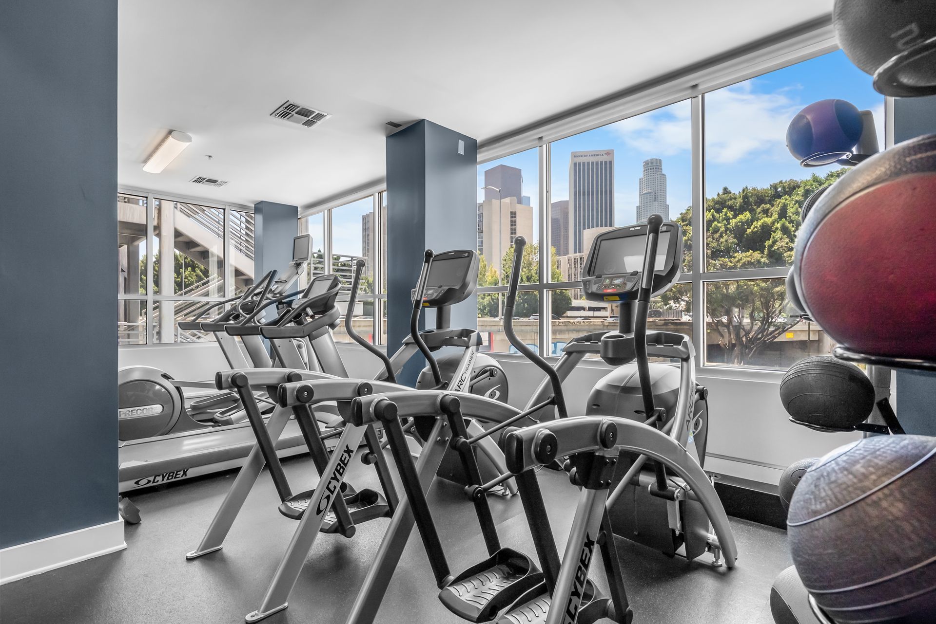 Elliptical machines and a treadmill in front of a window overlooking skyscrapers 