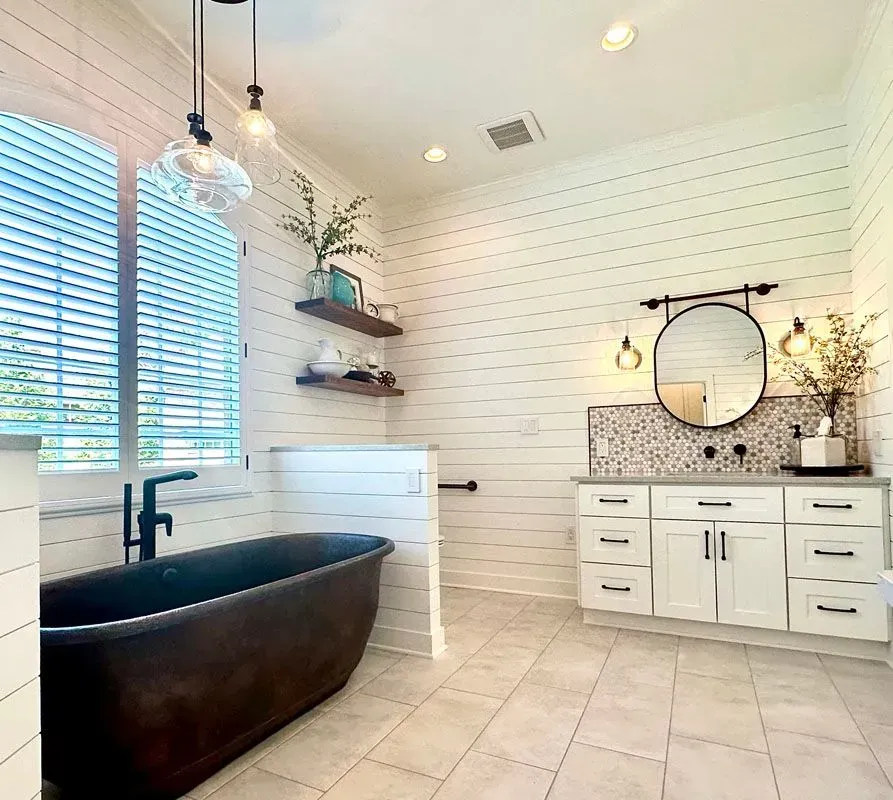 A bathroom with a black tub , sink , mirror and blinds.