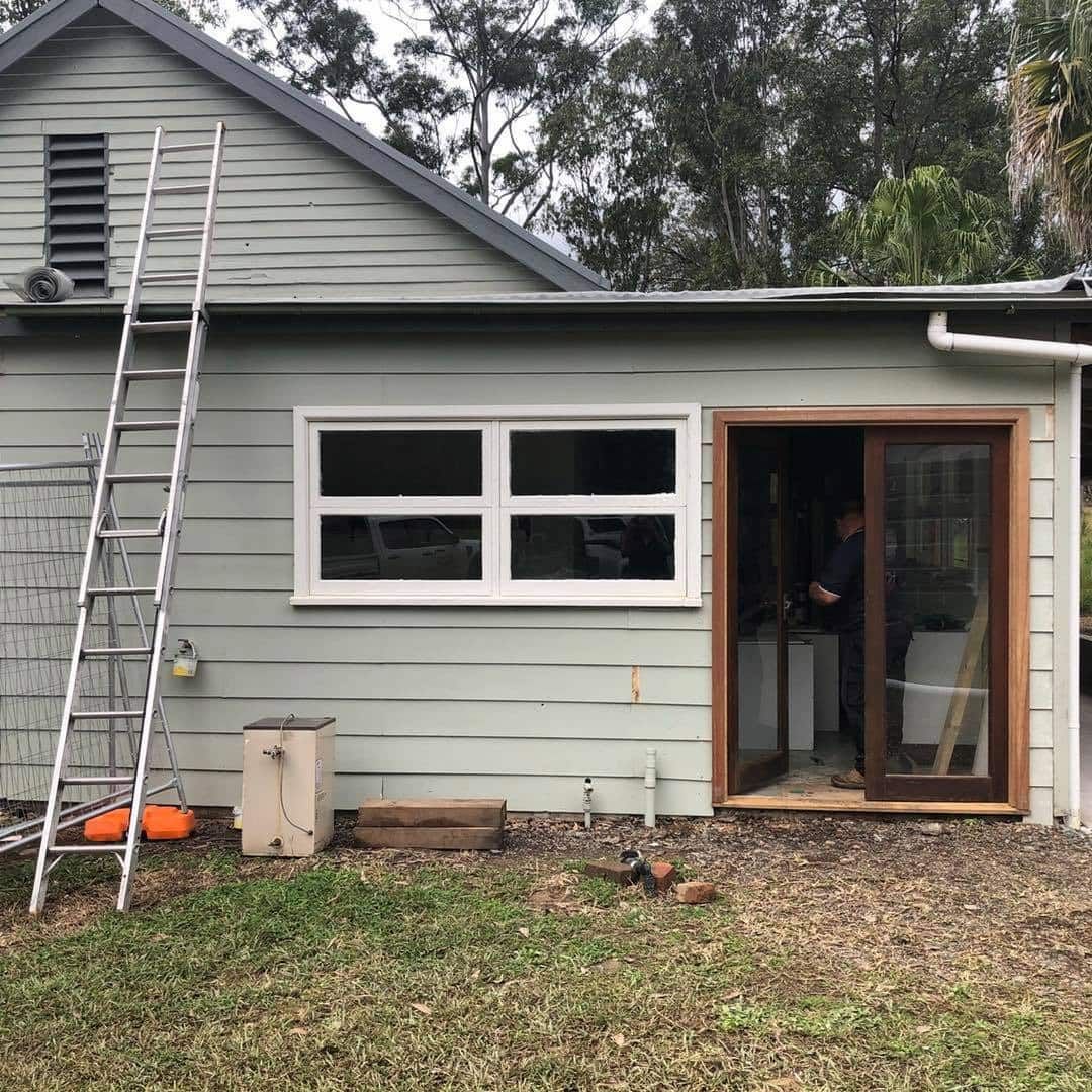 A Light Green Building With a Window, Doorway, and Ladder — Alcando Renovations and Maintenance in Bobin, NSW