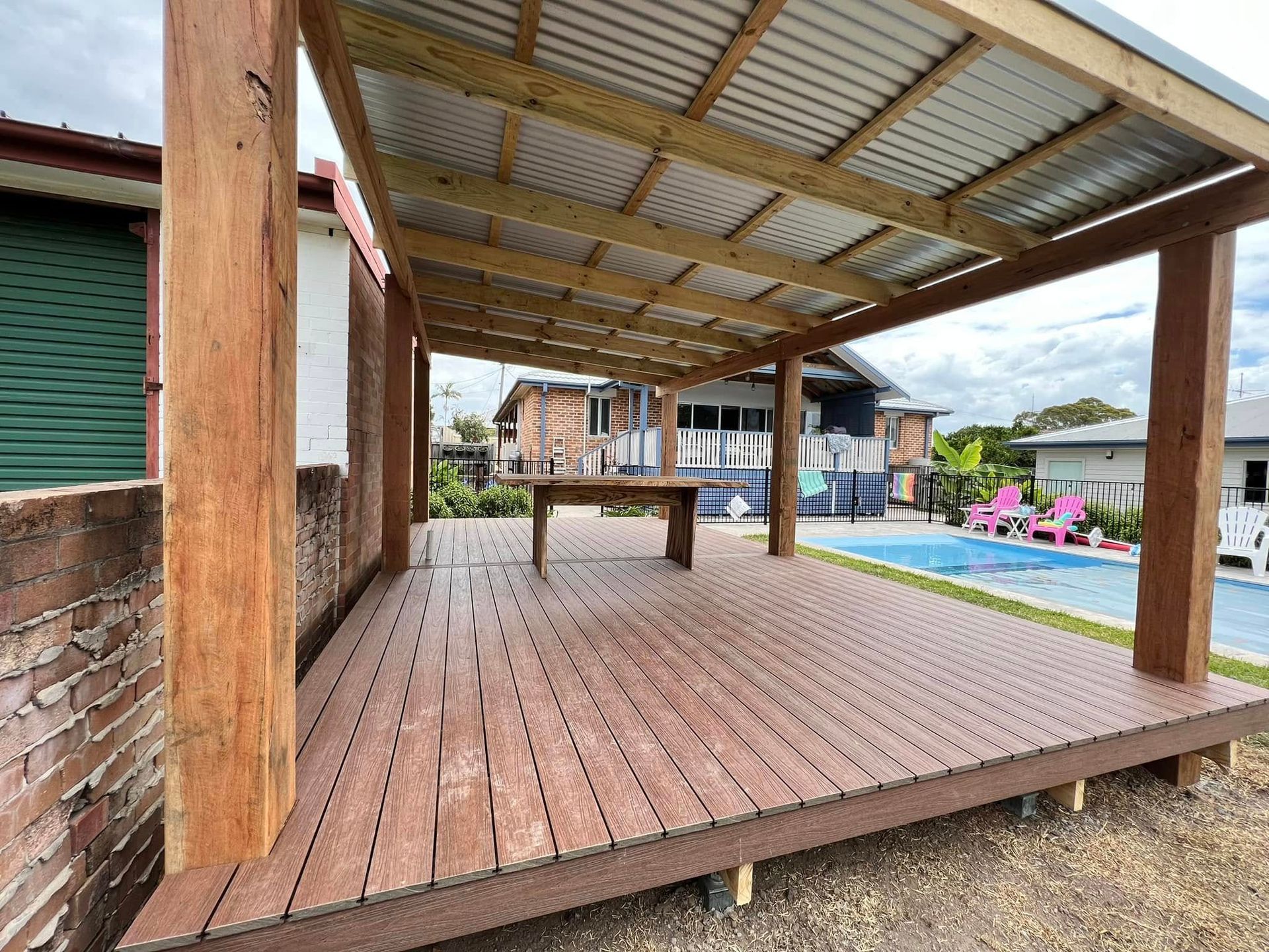 Covered Wooden Deck With Table, Pool, and Residential Backdrop — Alcando Renovations and Maintenance In Taree, NSW