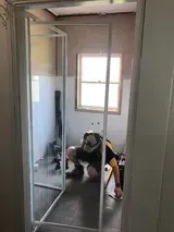 Man Installs Shower Door in Bathroom, Crouched on Floor — Alcando Renovations and Maintenance In Bobin, NSW