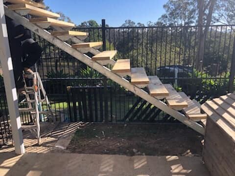 Person on Ladder Building Outdoor Wooden Stairs Against a Fence — Alcando Renovations and Maintenance In Bobin, NSW