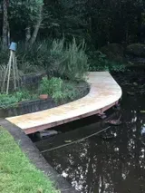 Wooden Boardwalk Curving Over a Dark Pond in a Garden Setting — Alcando Renovations and Maintenance In Bobin, NSW
