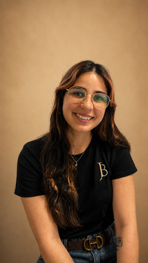 Smiling person with glasses in a black shirt against a beige background